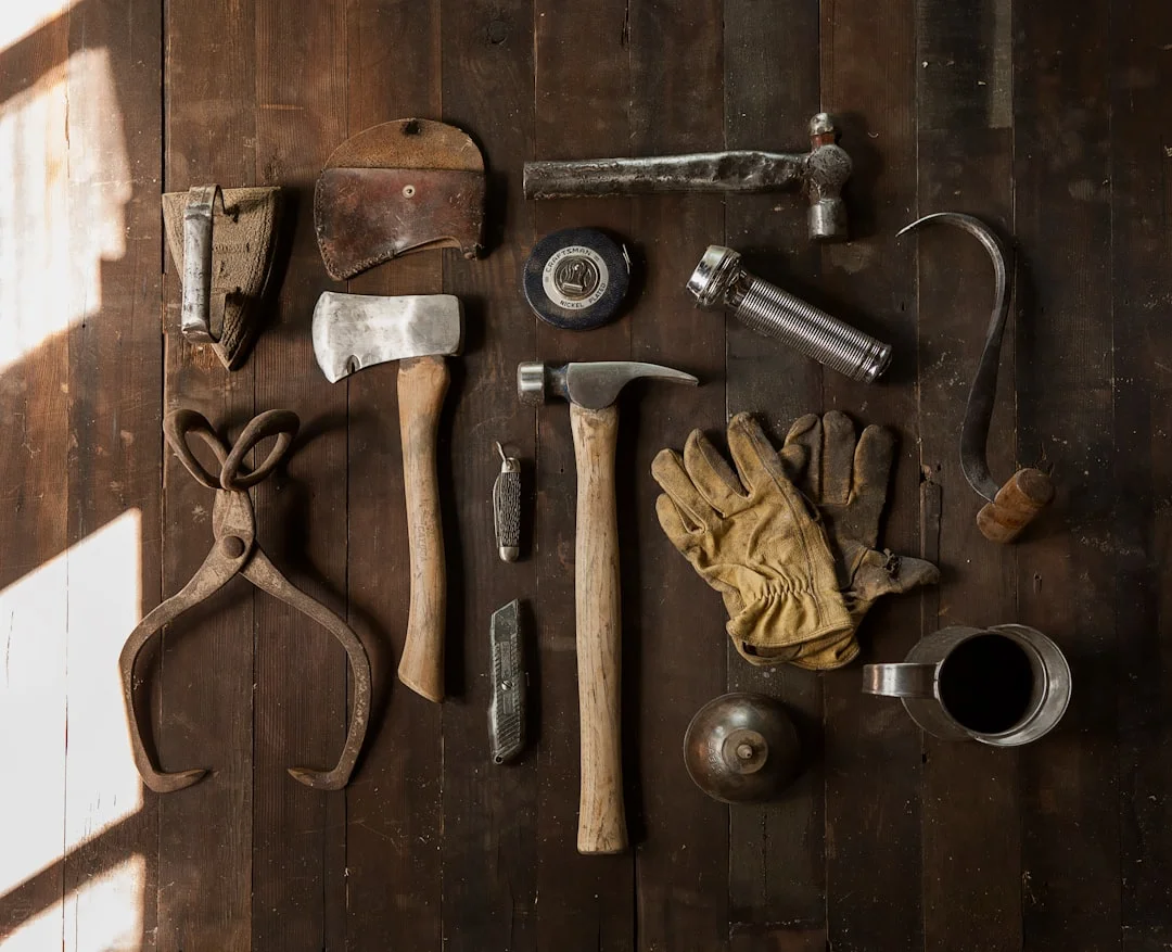 A well-lit garage workshop with a cabinet table saw in the foreground, hand planes on the wall, and sawdust on a concrete floor — a craftsperson mid-cut on a hardwood panel